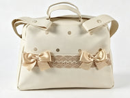 Cream faux leather handbag with a top handle, shoulder strap, decorative polka dots, and two beige satin bows with a lace trim across the front.
