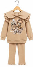 Load image into Gallery viewer, A toddler girl's two-piece beige sweatshirt and pants set hanging on a wooden hanger. The sweatshirt features a large ruffled Peter Pan collar with a matching bow, a central graphic of a teddy bear and a lantern, and ruffled cuffs and hem.