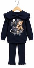 Load image into Gallery viewer, A toddler girl's two-piece navy blue outfit set consisting of a long-sleeve top with a large ruffled collar and bow, featuring a teddy bear and perfume bottle applique on the front, paired with matching ruffled flare pants, shown on a wooden hanger against a white background.